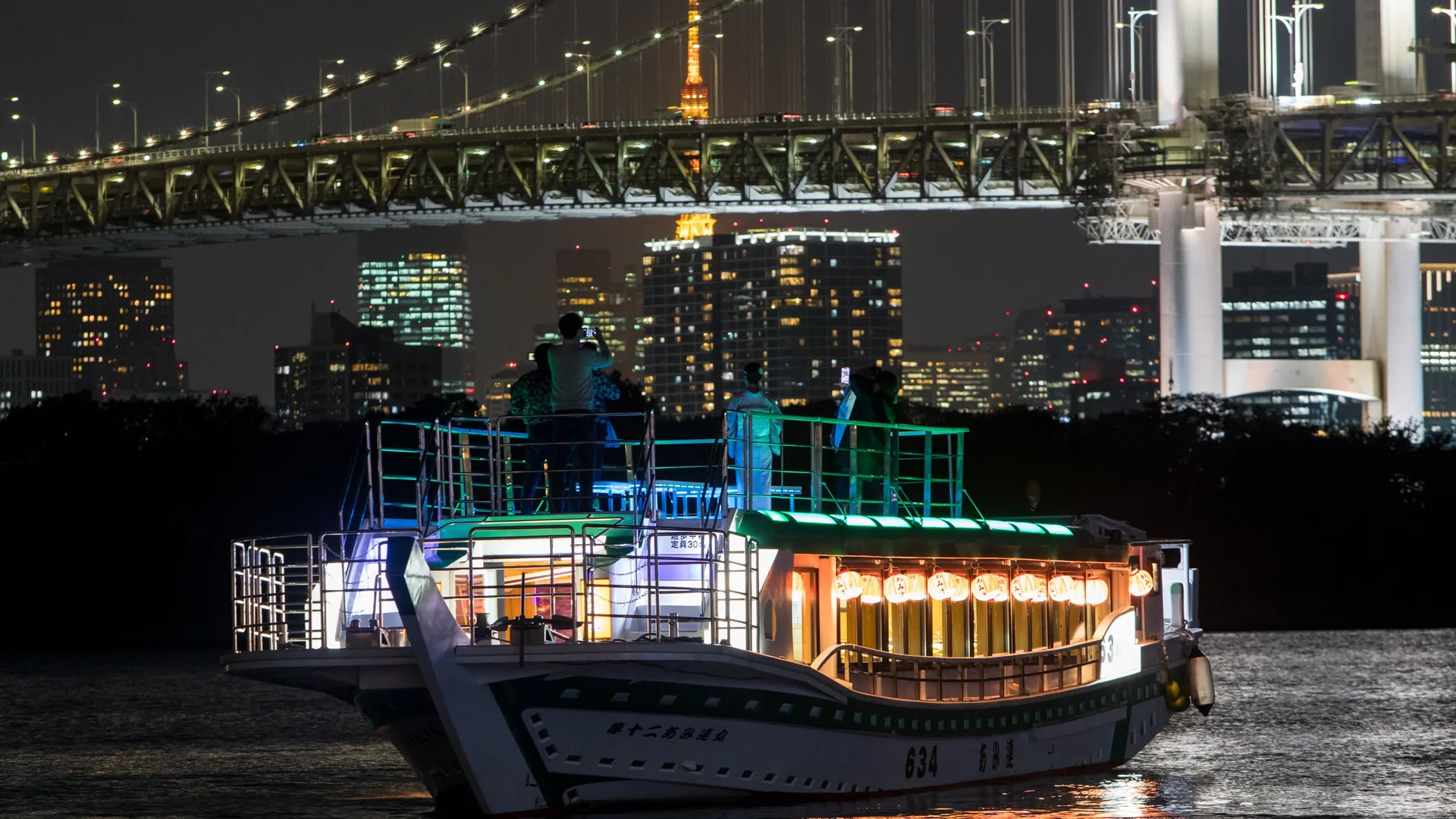Amitatsu's yakatabune lit up at night on Tokyo Bay with the Rainbow Bridge and Tokyo Tower behind, from the Sumida River cruise listing