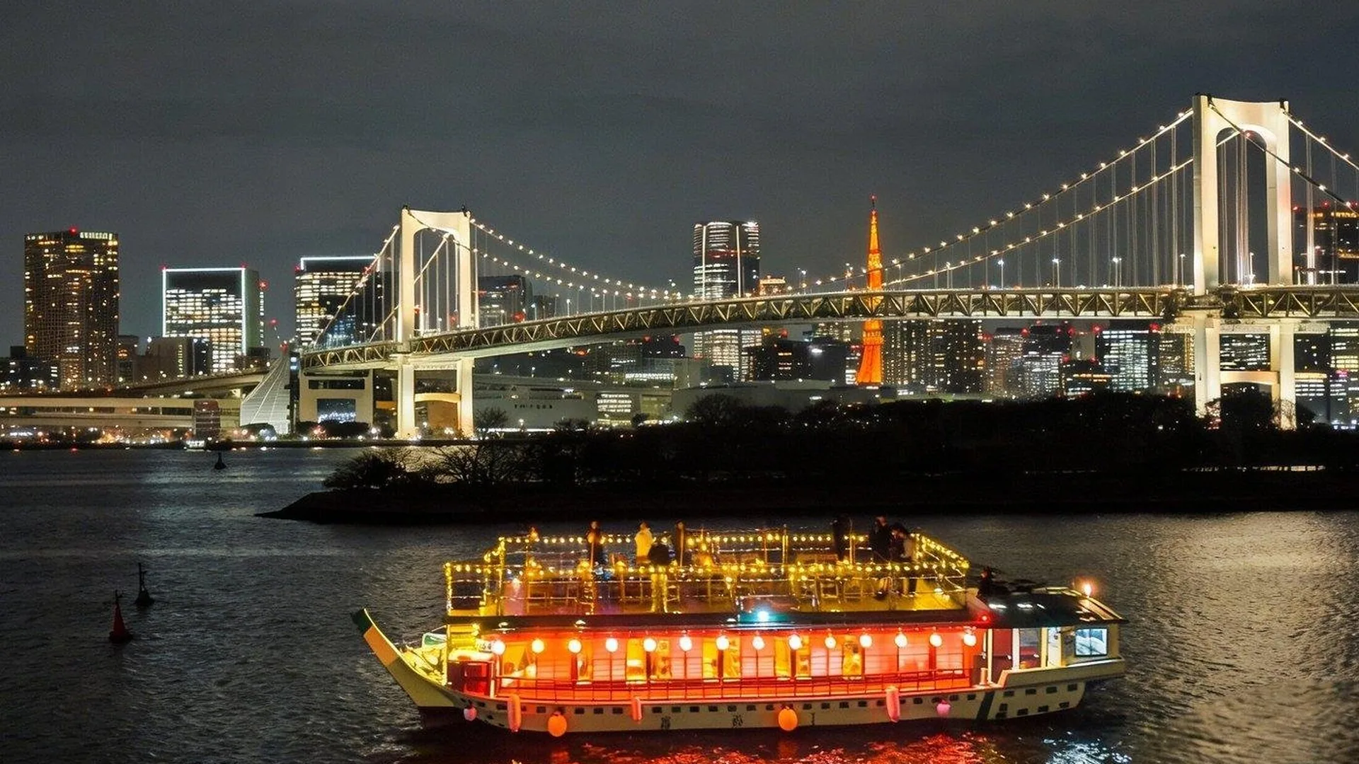 A lit yakatabune on Tokyo Bay in front of the illuminated Rainbow Bridge, from the Tokyo Bay cruise listing
