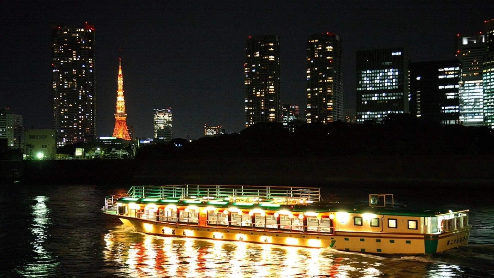 A yakatabune houseboat lit up at night on the water with Tokyo Tower behind, from the H.I.S. cruise listing